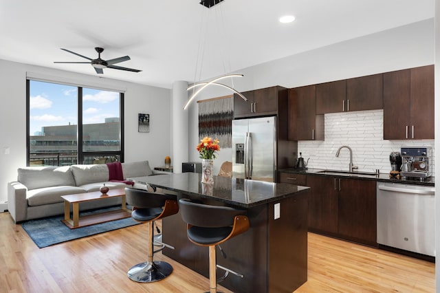 kitchen featuring sink, light wood-type flooring, a kitchen island, hanging light fixtures, and stainless steel appliances