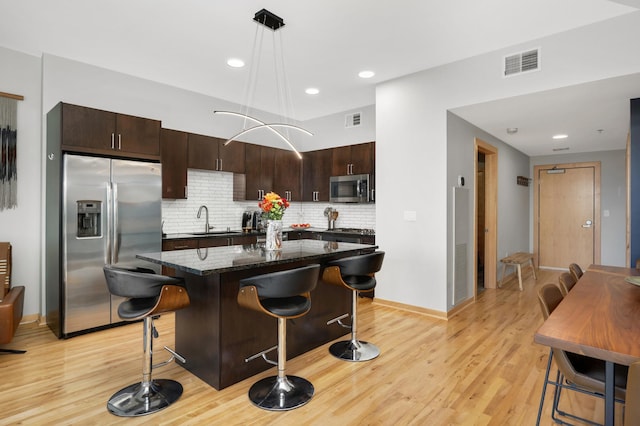 kitchen with tasteful backsplash, appliances with stainless steel finishes, light wood-type flooring, sink, and decorative light fixtures