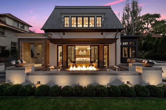 back house at dusk featuring a patio, an outdoor fire pit, and a fireplace