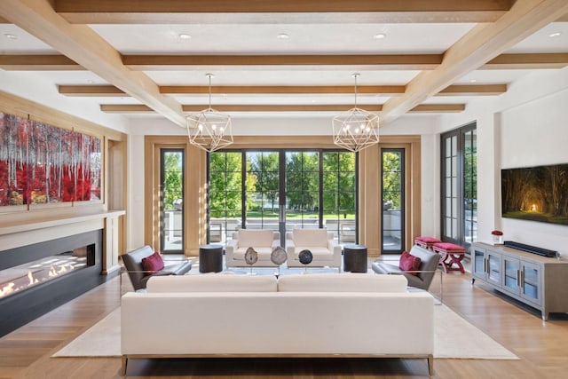 living room with a notable chandelier, beamed ceiling, plenty of natural light, and light wood-type flooring