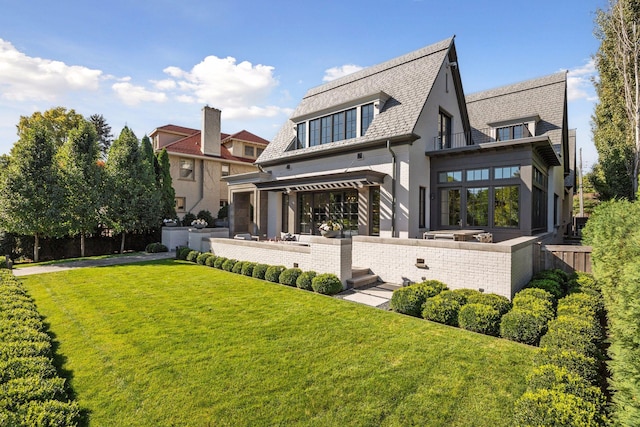 rear view of house with a balcony, a patio, and a lawn