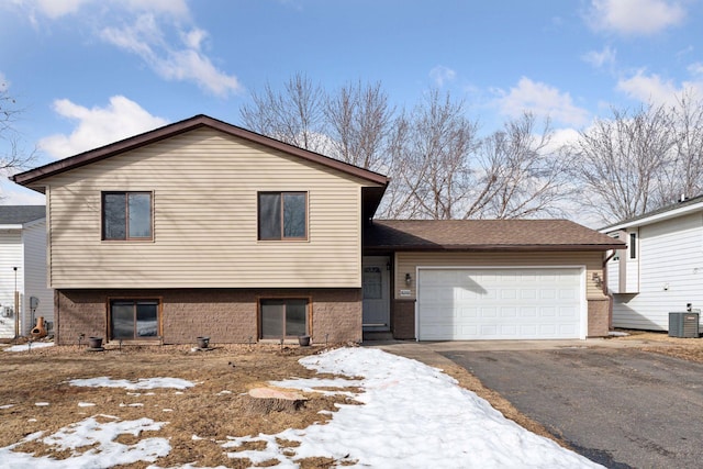 tri-level home with aphalt driveway, central AC unit, brick siding, and a garage