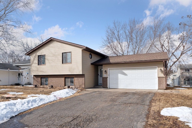 split level home with aphalt driveway, a garage, and brick siding