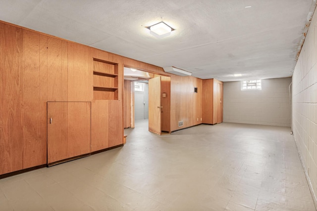 basement featuring light floors, visible vents, wood walls, and concrete block wall