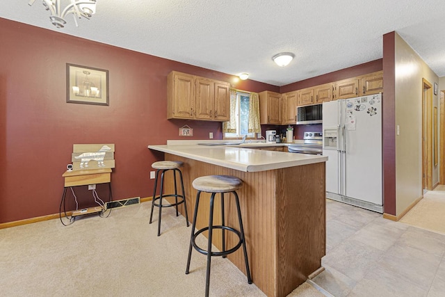 kitchen featuring a textured ceiling, stainless steel appliances, a breakfast bar area, light brown cabinets, and light colored carpet