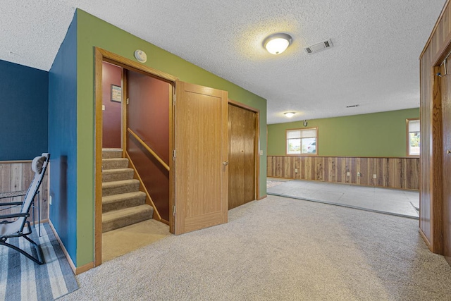 hallway featuring wooden walls, a textured ceiling, and light colored carpet