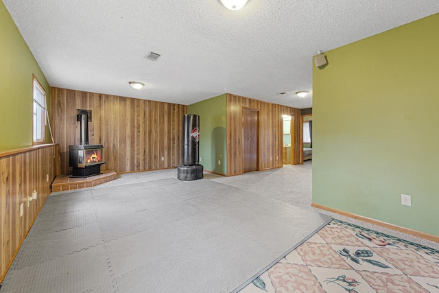 unfurnished living room featuring a textured ceiling, a wood stove, and wood walls