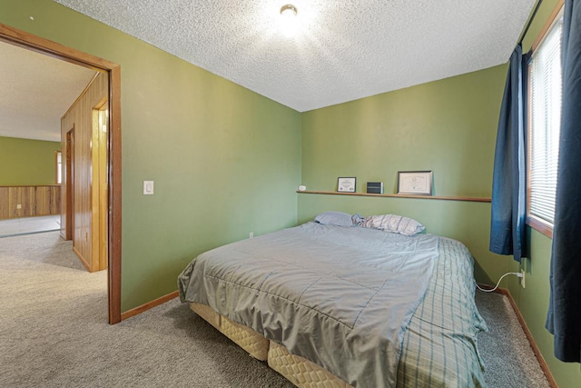 bedroom featuring light carpet, a textured ceiling, and wooden walls