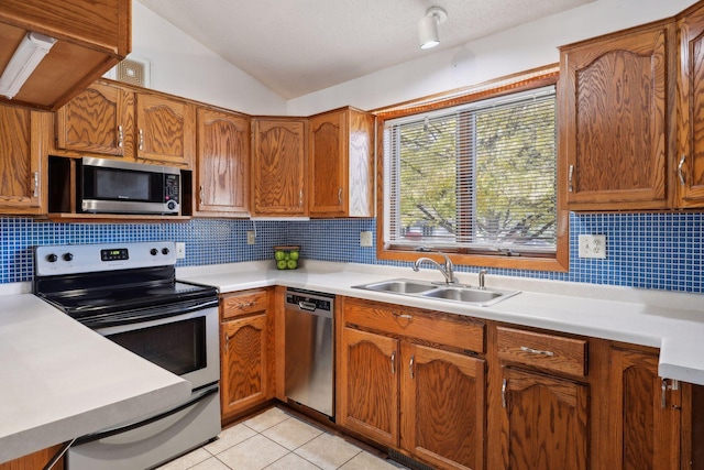 kitchen with lofted ceiling, backsplash, light tile patterned flooring, sink, and stainless steel appliances