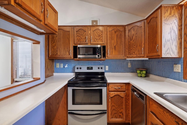 kitchen featuring sink, backsplash, appliances with stainless steel finishes, and lofted ceiling