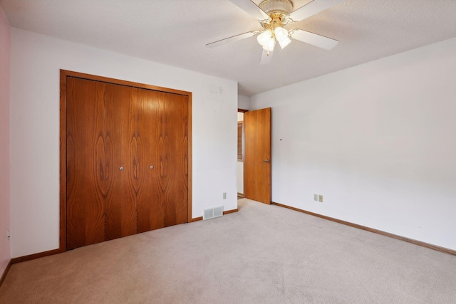 unfurnished bedroom featuring a textured ceiling, light colored carpet, a closet, and ceiling fan