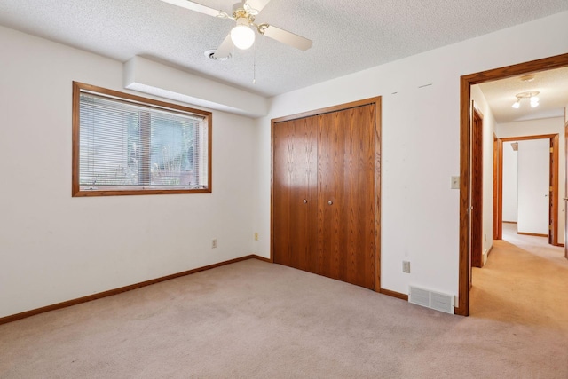 unfurnished bedroom with a closet, ceiling fan, a textured ceiling, and light colored carpet