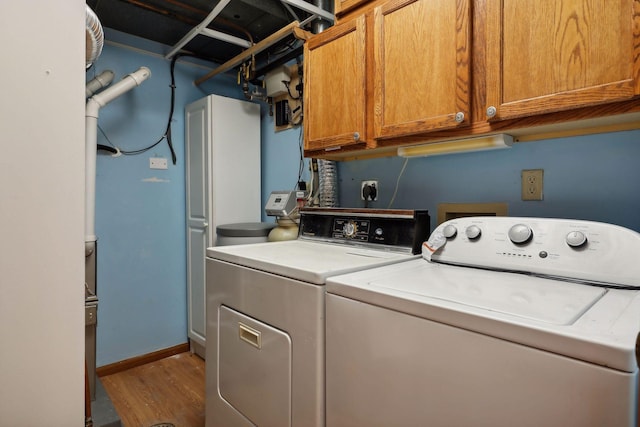 clothes washing area with hardwood / wood-style flooring, separate washer and dryer, and cabinets