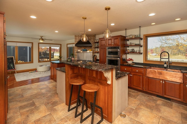 kitchen featuring stainless steel double oven, a center island, a kitchen bar, decorative light fixtures, and ceiling fan