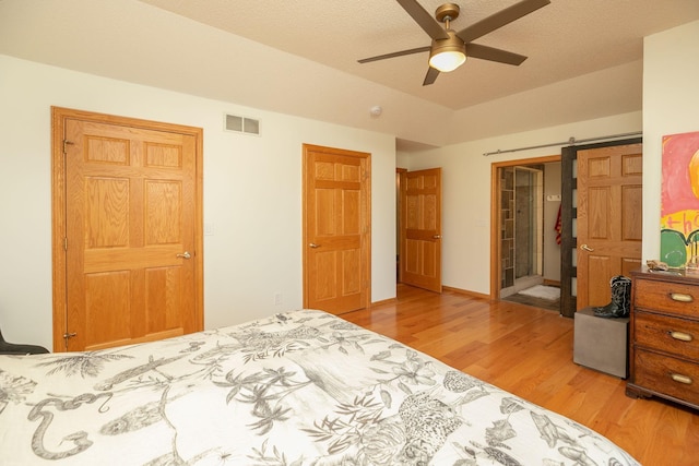 bedroom featuring ceiling fan, a textured ceiling, light hardwood / wood-style flooring, and a barn door