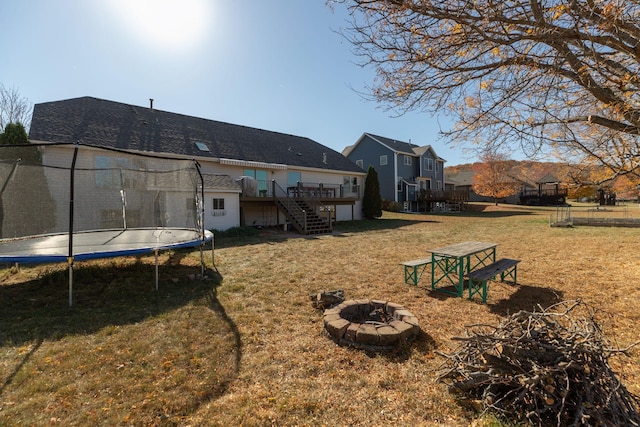 back of property with a yard, a fire pit, a wooden deck, and a trampoline