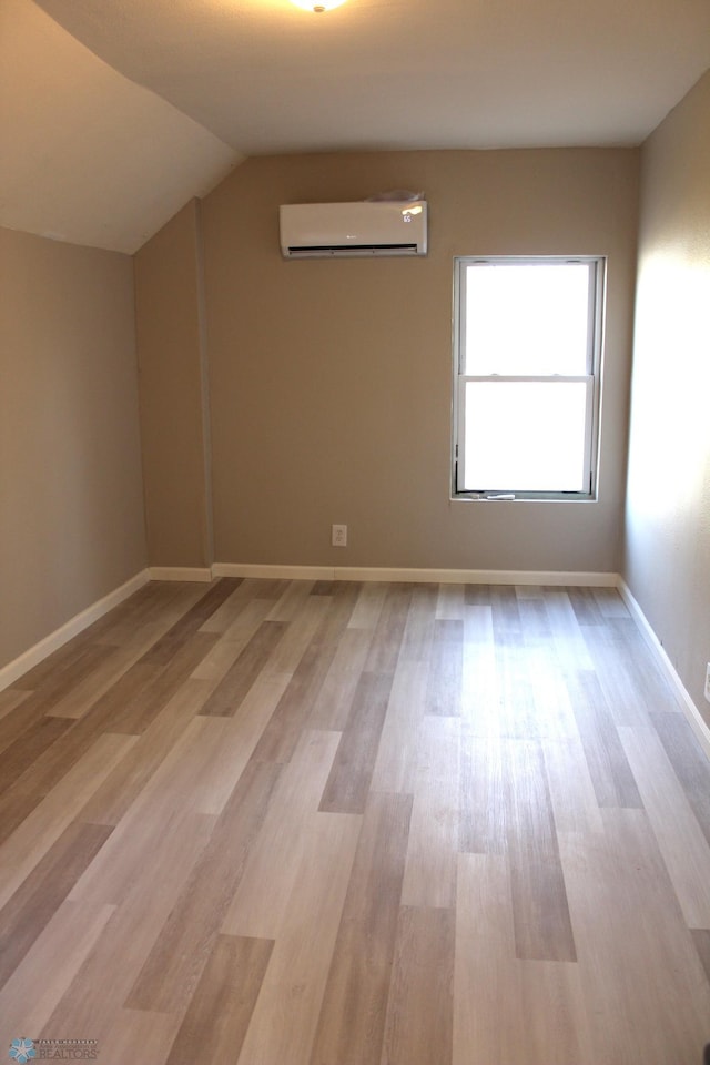 additional living space featuring vaulted ceiling, light hardwood / wood-style flooring, and a wall unit AC