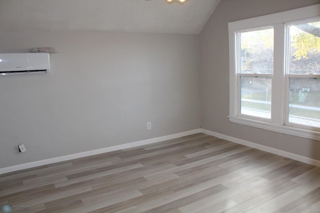 additional living space with lofted ceiling, a wall unit AC, and light wood-type flooring