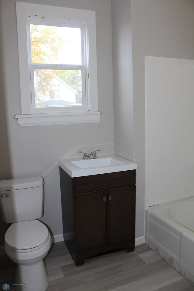 bathroom featuring vanity, wood-type flooring, toilet, and a washtub