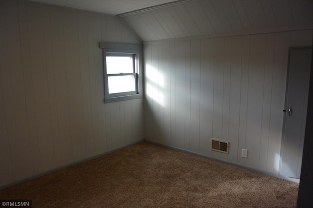 carpeted empty room with lofted ceiling and wooden walls