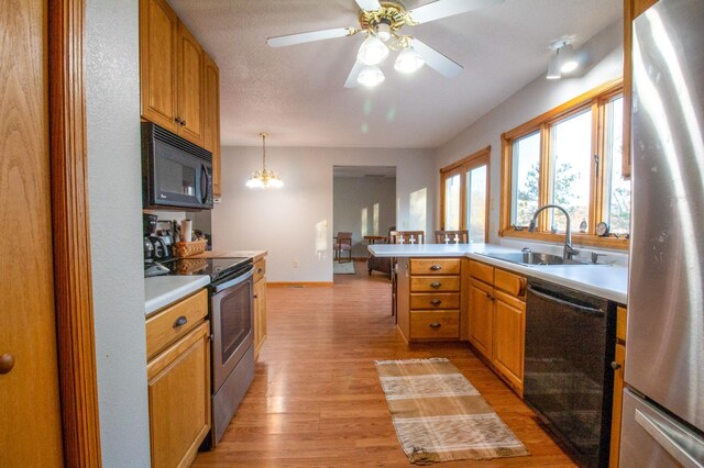 kitchen with sink, black appliances, decorative light fixtures, light wood-type flooring, and ceiling fan with notable chandelier