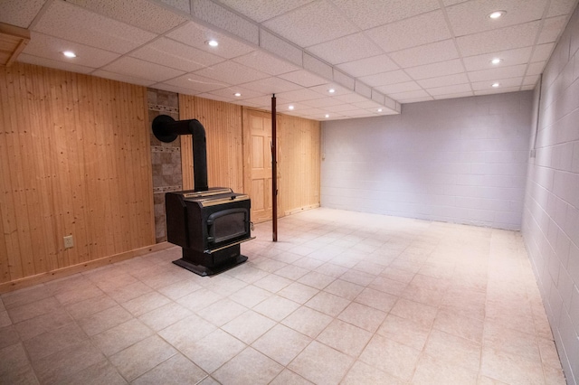 basement with wooden walls, a paneled ceiling, and a wood stove