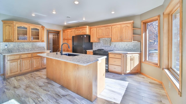 kitchen featuring decorative backsplash, a kitchen island with sink, black appliances, and plenty of natural light