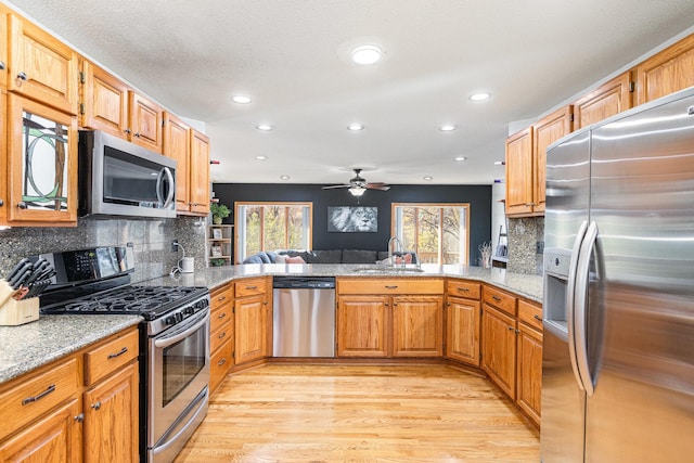 kitchen with appliances with stainless steel finishes, light hardwood / wood-style flooring, sink, and kitchen peninsula