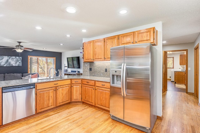 kitchen with appliances with stainless steel finishes, sink, light wood-type flooring, kitchen peninsula, and ceiling fan