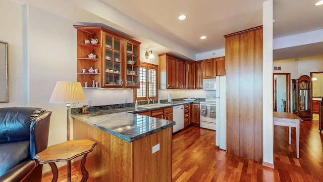 kitchen featuring kitchen peninsula, dark wood-type flooring, dark stone counters, and white appliances