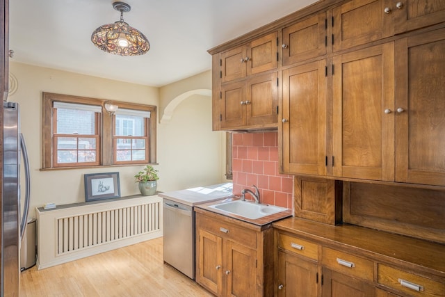 kitchen featuring sink, hanging light fixtures, light hardwood / wood-style flooring, appliances with stainless steel finishes, and tasteful backsplash