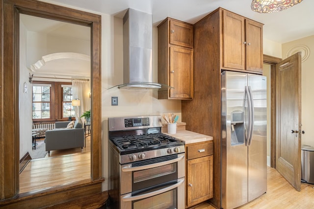 kitchen with stainless steel appliances, light hardwood / wood-style flooring, and wall chimney exhaust hood