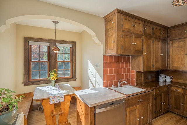 kitchen with sink, dishwasher, hanging light fixtures, tasteful backsplash, and light hardwood / wood-style floors