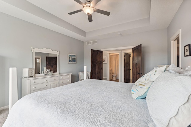 bedroom featuring carpet flooring, ensuite bathroom, a tray ceiling, and ceiling fan