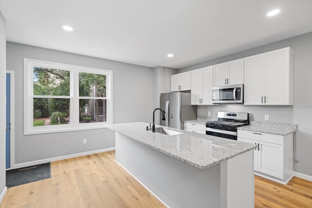 kitchen with white cabinetry, appliances with stainless steel finishes, light wood-type flooring, and a center island with sink