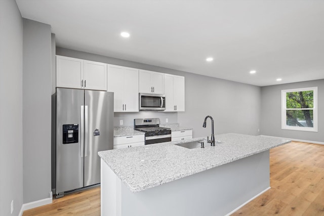 kitchen with light hardwood / wood-style floors, stainless steel appliances, sink, and a center island with sink