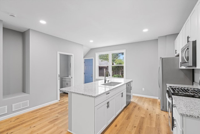 kitchen featuring white cabinets, a center island with sink, appliances with stainless steel finishes, light wood-type flooring, and sink