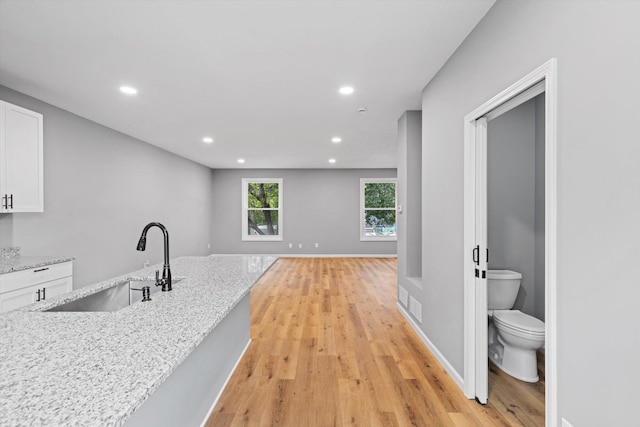 kitchen with sink, light stone countertops, light hardwood / wood-style floors, and white cabinets