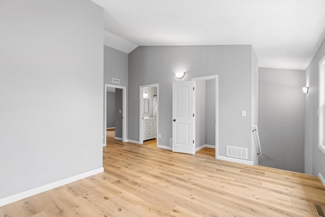 unfurnished bedroom with light hardwood / wood-style flooring, connected bathroom, and vaulted ceiling