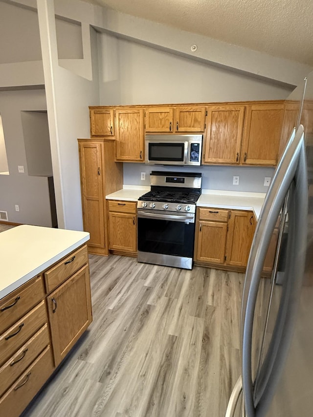 kitchen featuring a textured ceiling, stainless steel appliances, light hardwood / wood-style flooring, and lofted ceiling