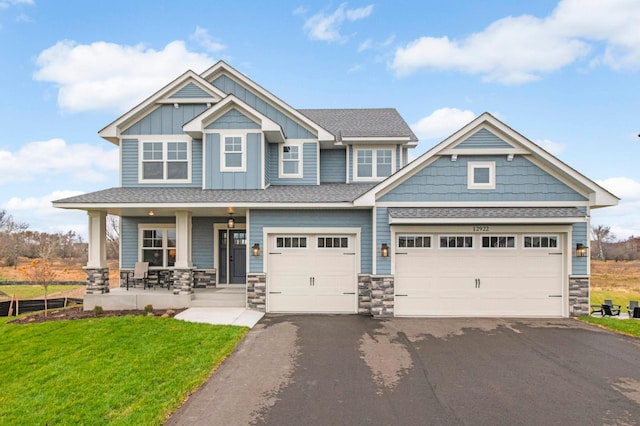 craftsman inspired home featuring a porch, a front lawn, and a garage