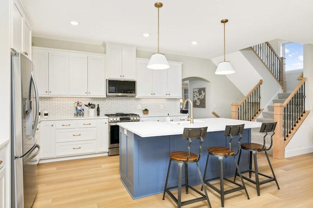 kitchen with white cabinets, appliances with stainless steel finishes, an island with sink, and hanging light fixtures