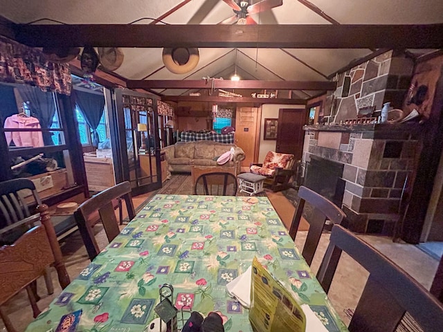 dining space with ceiling fan, a stone fireplace, and lofted ceiling with beams