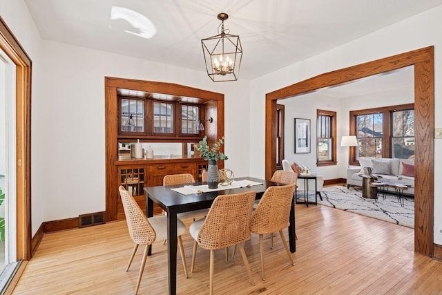 dining room featuring light wood-style flooring, a notable chandelier, baseboards, and visible vents