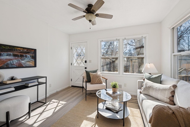 living area featuring light wood-style floors, baseboards, and ceiling fan