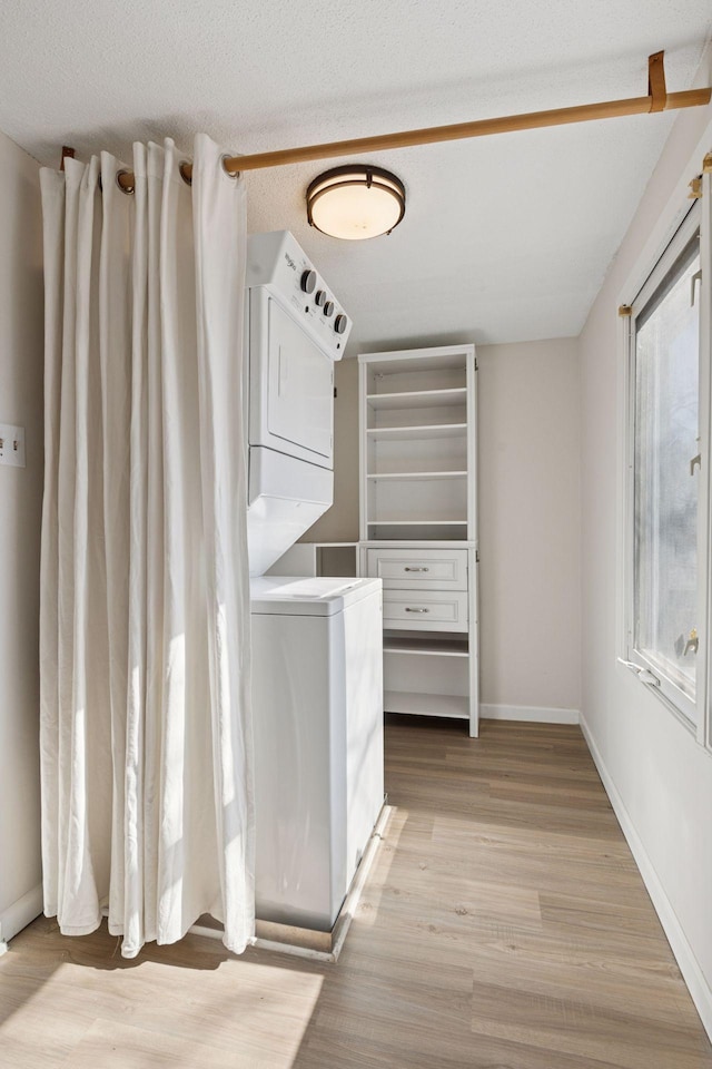 clothes washing area with baseboards, stacked washer and dryer, light wood-style flooring, and laundry area