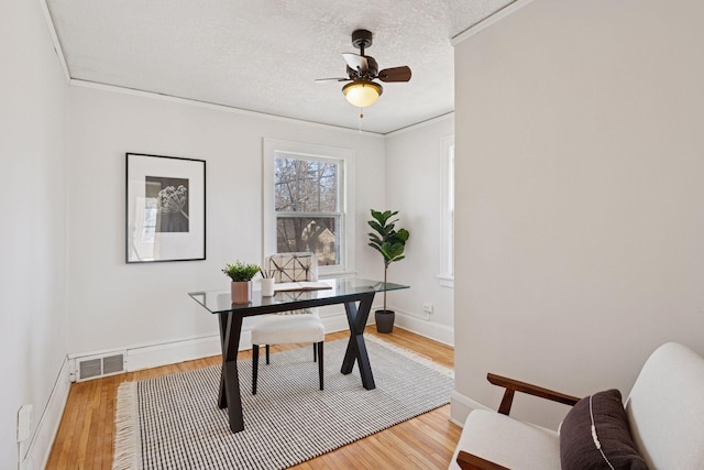 home office featuring a ceiling fan, visible vents, light wood-style floors, a textured ceiling, and crown molding