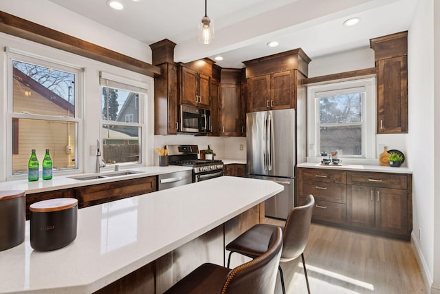 kitchen featuring light wood-style flooring, a sink, hanging light fixtures, light countertops, and stainless steel appliances