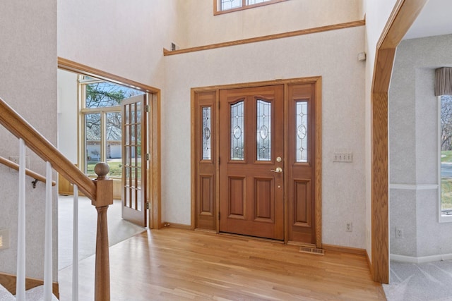 foyer entrance with plenty of natural light, light wood-style flooring, and a towering ceiling