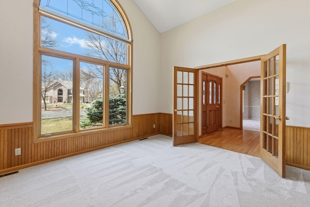 carpeted empty room with high vaulted ceiling, wainscoting, and french doors